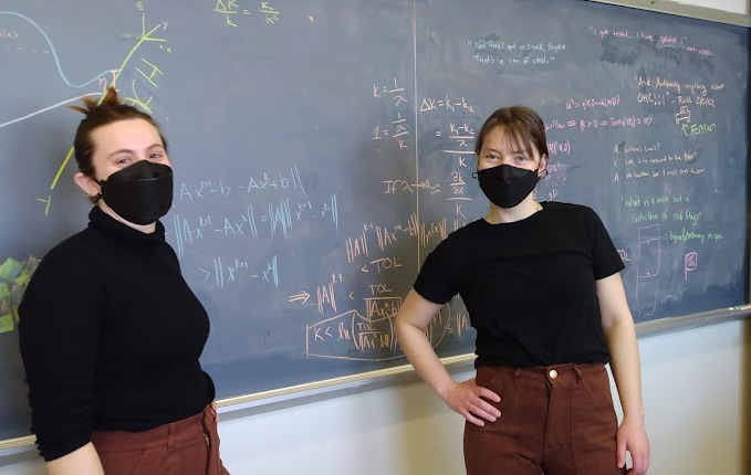 Brynn and Elena in matching outfits in front of a chalkboard with math